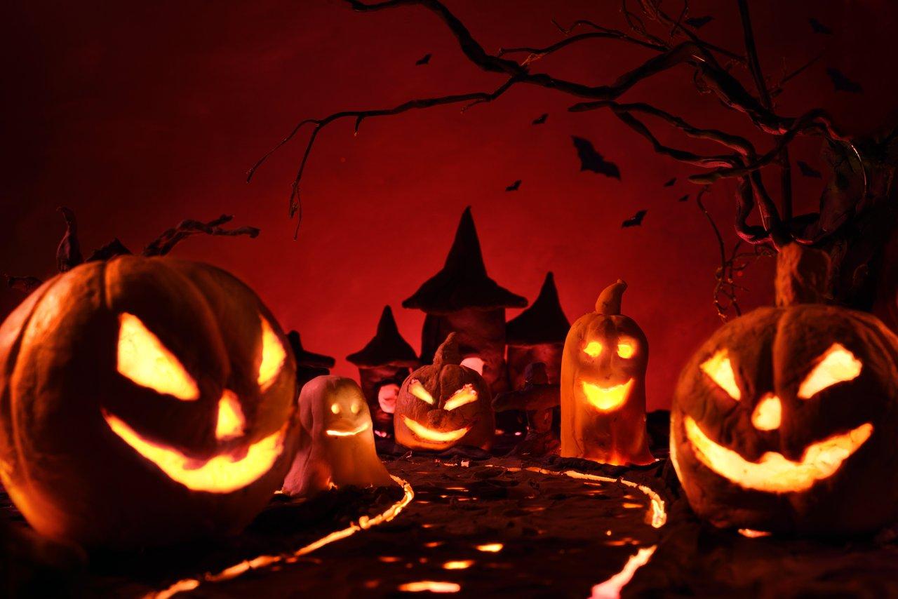 Parc à thème Halloween la nuit : ambiance mystérieuse, éclairages colorés et visiteurs en costumes.