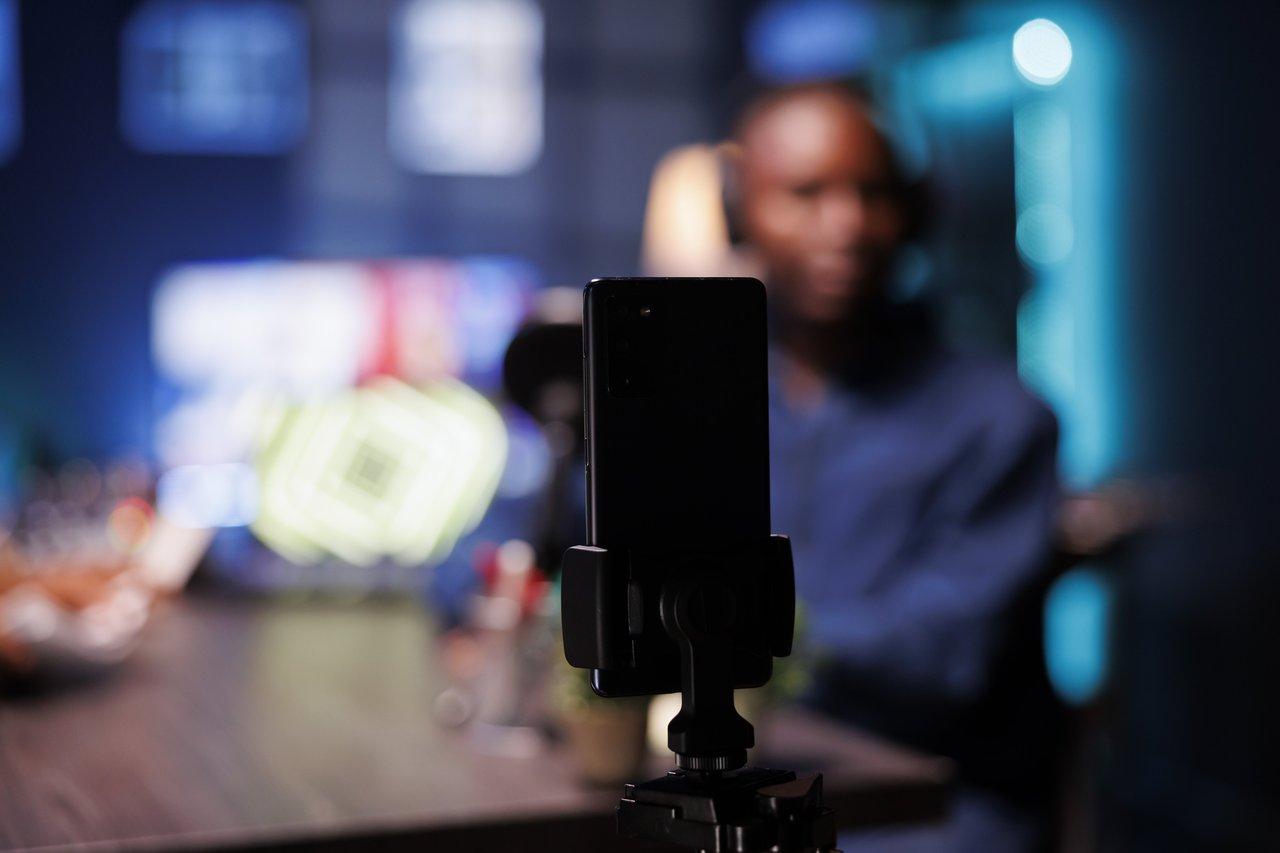 Smartphone en cours de montage vidéo pour YouTube Shorts dans un studio avec un vlogger en arrière-plan.